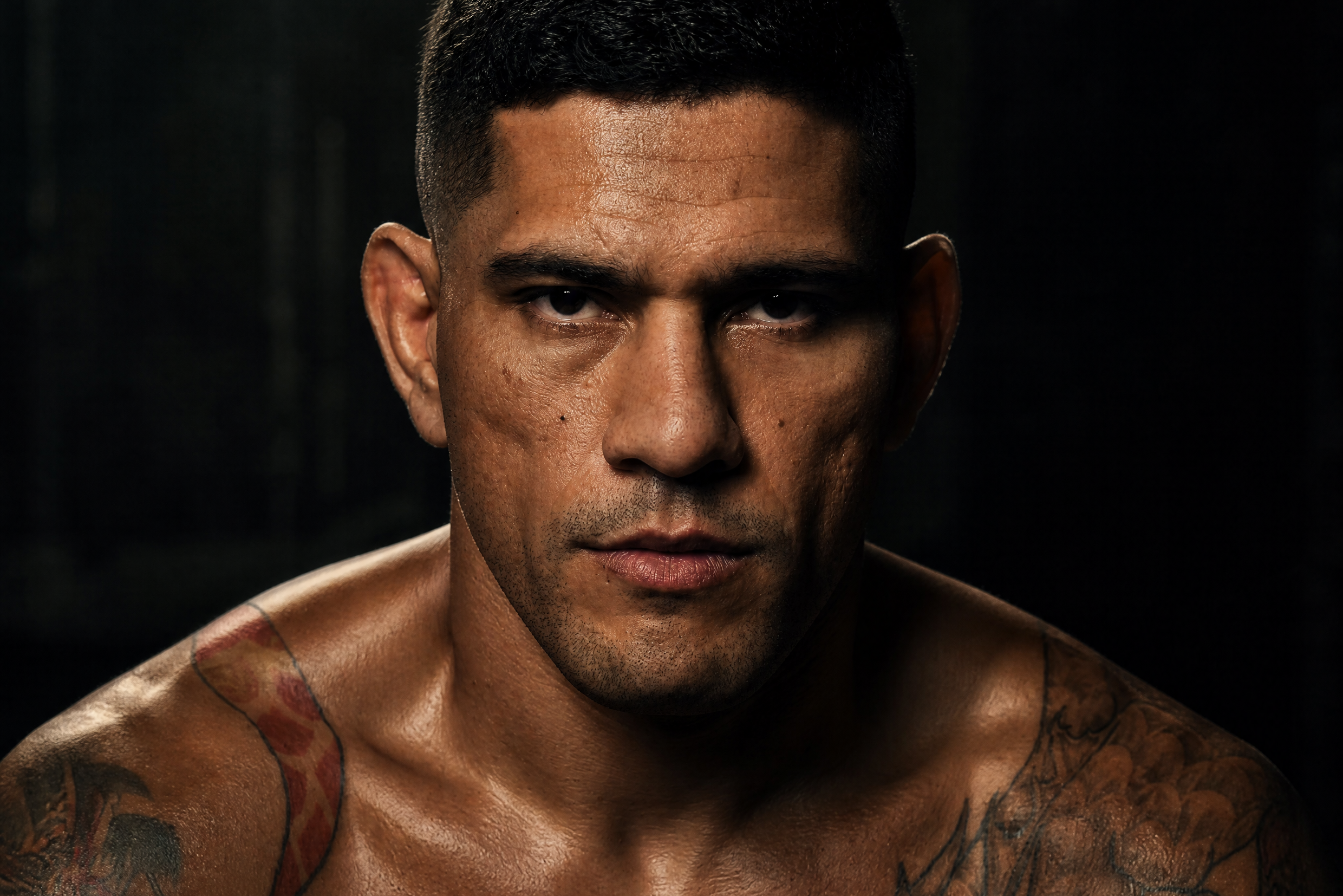 Alex Pereira with tattoos on his arms and chest against a dark background